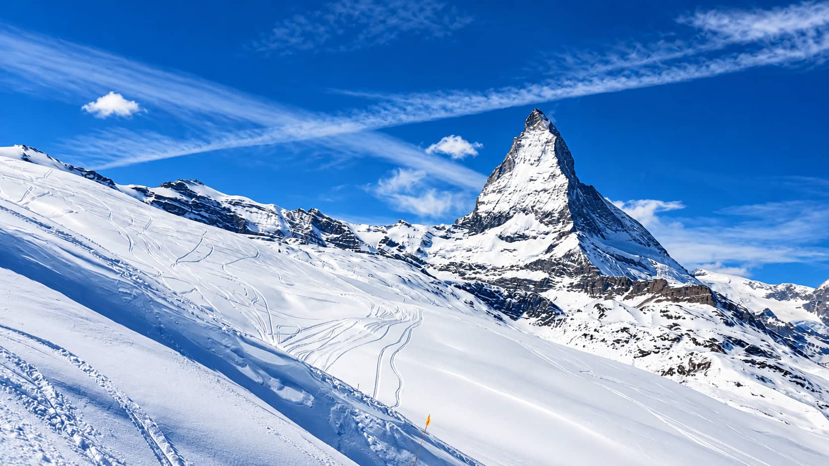 The Matterhorn under a deep blue sky, above snowy slopes with ski tracks.
