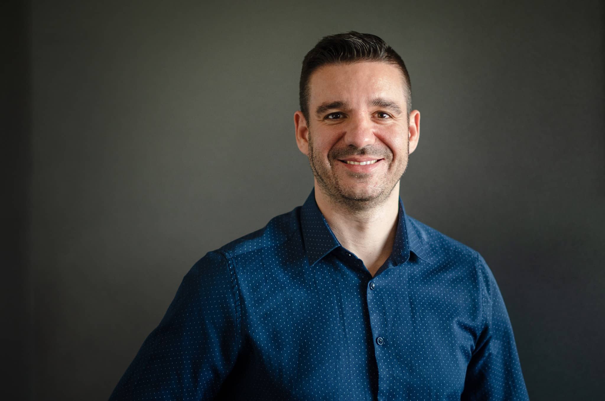 Stanislav Popov smiling in a navy patterned shirt against a dark grey background.