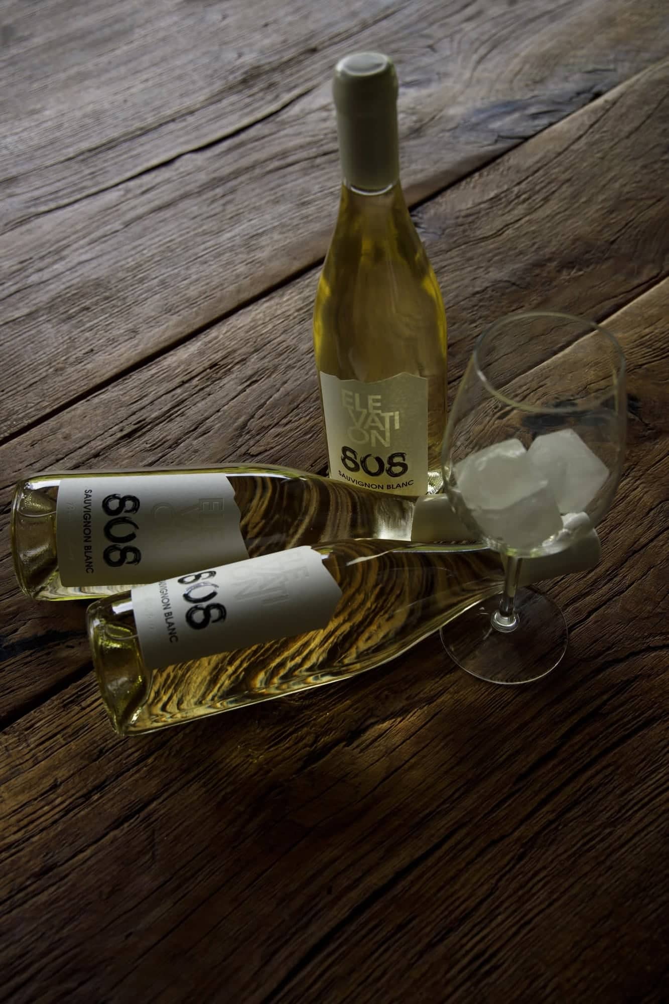 Bottles of Elevation 808 Sauvignon Blanc lying on weathered oak boards beside a glass with ice.